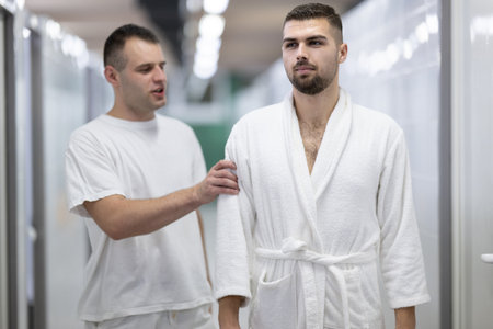 Medical Consultation in Spa Corridor.Two men discussing treatment options while walking through a clinical spa corridor, wearing white uniforms and bathrobe.の写真素材
