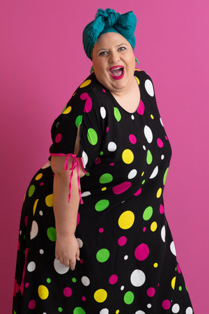 Colorful expressive big size woman posing in polka dot dress on pink backgroundの写真素材