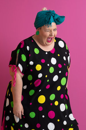 Colorful expressive big size woman posing in polka dot dress on pink backgroundの写真素材