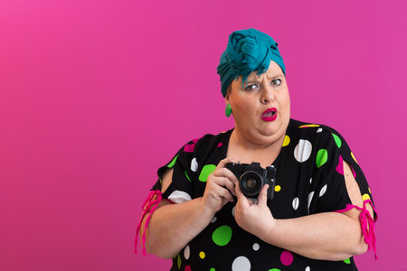 Surprised woman holding camera on pink backgroundの写真素材