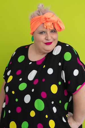Plus size woman in vibrant polka dot outfit making a comic shrug gesture with outstretched hands and amusing expression.の写真素材