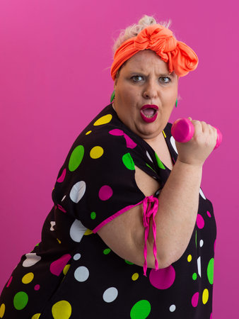 Surprised plus size woman exercising with pink dumbbells on colorful backgroundの写真素材