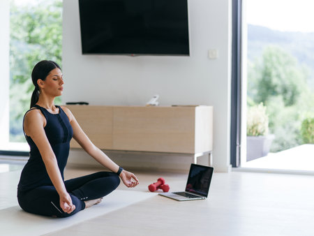 Young Beautiful Female Exercising, Stretching and Practising Yoga with Trainer via Video Call Conference in Bright Sunny House. Healthy Lifestyle, Wellbeing and Mindfulness Concept.の写真素材