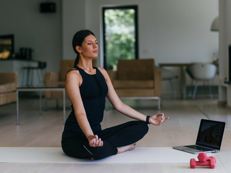 Young Beautiful Female Exercising, Stretching and Practising Yoga with Trainer via Video Call Conference in Bright Sunny House. Healthy Lifestyle, Wellbeing and Mindfulness Concept.の写真素材