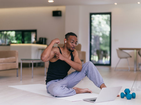Training At Home. Sporty man doing the training while watching an online tutorial on a laptop, exercising in the living room, free space.の写真素材
