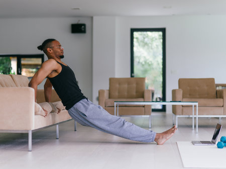 Training At Home. Sporty man doing the training while watching an online tutorial on a laptop, exercising in the living room, free space.の写真素材