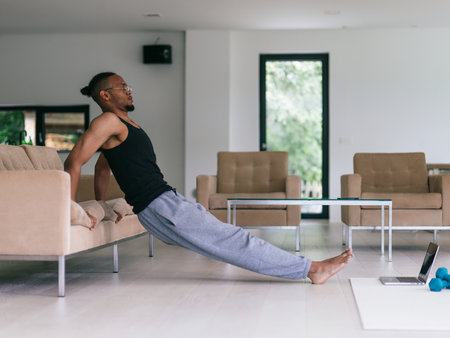 Training At Home. Sporty man doing the training while watching an online tutorial on a laptop, exercising in the living room, free space.の写真素材
