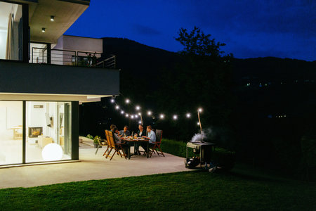 A group of young diverse people having dinner on the terrace of a modern house in the evening. Fun...