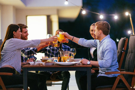A group of young diverse people having dinner on the terrace of a modern house in the evening. Fun...