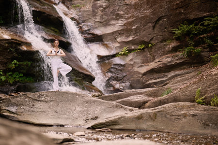 Woman doing yoga tree pose in front of waterfall at sunrise peaceful meditation in natureの写真素材