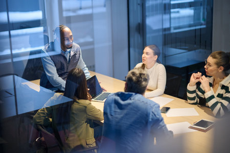 Diverse business team gathered around a table discussing analytics during a meeting in a modern office. Laptop screen shows charts and graphs, symbolizing teamwork, communication, and data driven strategy.の写真素材