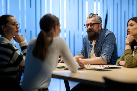 Group of diverse coworkers having a serious discussion around a conference table, led by a bearded male manager, representing teamwork, leadership, and strategy development in a modern business environment.の写真素材