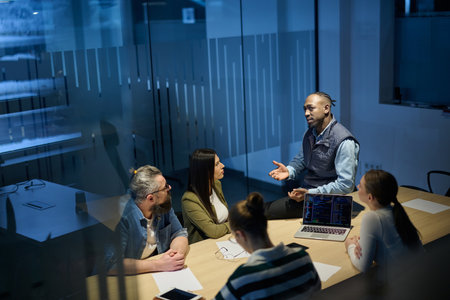 Diverse business team gathered around a table discussing analytics during a meeting in a modern office. Laptop screen shows charts and graphs, symbolizing teamwork, communication, and data driven strategy.の写真素材