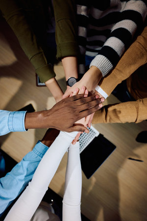Top view of diverse coworkers business people joining hands together over a wooden office desk,...