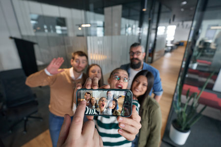 Group of cheerful coworkers taking a selfie together in a modern office environment. Concept of teamwork, friendship, success, and positive company culture.の写真素材