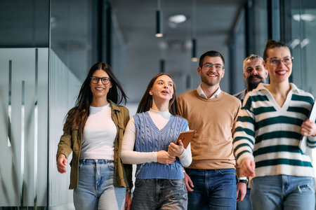 Group of young business team walking together through a modern office hallway, smiling and discussing work. Concept of confidence, teamwork, leadership, and positive workplace culture.の写真素材