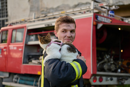 Brave firefighter holding a rescued cat in front of a fire engine, showcasing heroism and...