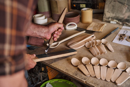 Craftsman sharpening carving tool, wooden spoons in workshop, handmade craft, artisan woodworker, traditional carving, woodworking process, hobby and creative occupation, craftsmanshipの写真素材
