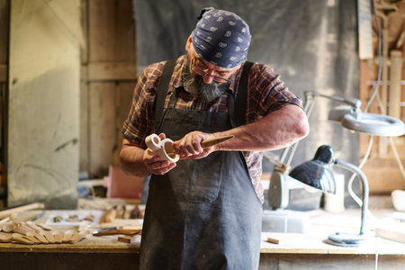 Craftsman shaping wooden toy in workshop, artisan carving wood, handmade crafts, woodworking, carpentry, hobby, small business, creative occupation, skilled labor, traditional craftの写真素材