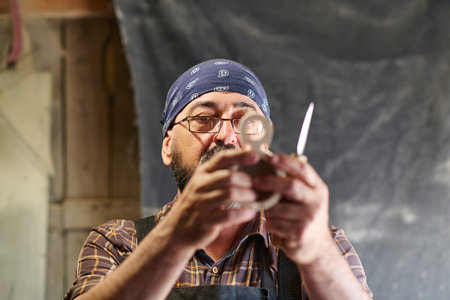Craftsman inspecting wooden figure eight with knife, artisan at work, woodworking project, handmade crafts, small business owner, creative hobby, art and craft workshop, indoor settingの写真素材