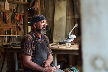 Craftsman carving wooden spoon in workshop, artisan working with wood, handmade craft, skilled artisan in studio, traditional woodworking, small business owner, creative hobby, craftsperson at workの写真素材