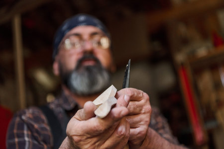 Man carving wood with a knife in workshop, craftsperson creating wooden figure, hobby and...