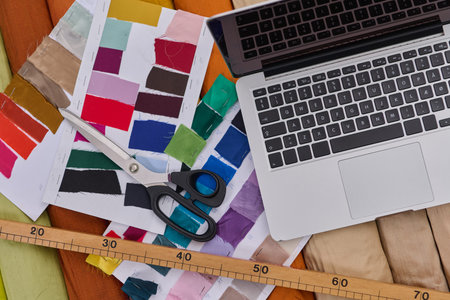 Fashion designers workspace with laptop, color swatches, scissors, measuring tape, and fabric,...