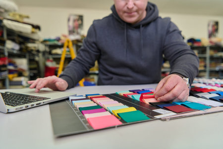 Fashion designer working with fabric swatches and laptop, designer selecting textile samples,...