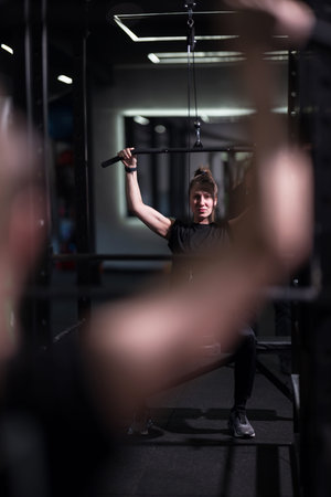 Woman lifting weights in a gym during a focused workout session with equipment and trainers in the...