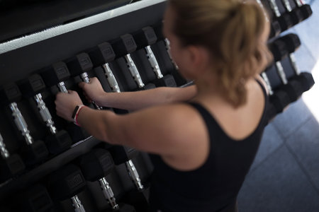 Woman selecting dumbbells at a gym during fitness training session in a well-lit exercise area