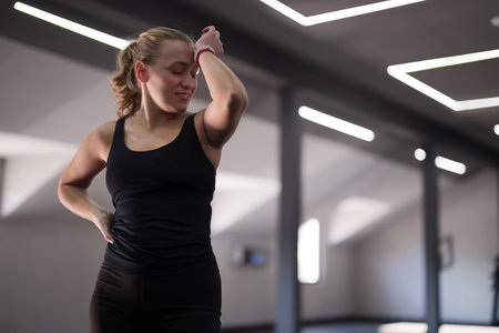 Woman in black workout attire resting and smiling during exercise session in modern gym with bright lightingの写真素材