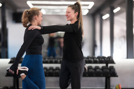 Two women engage in a friendly stretching exercise at a gym during a workout session in the morningの写真素材