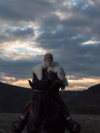 A Viking warrior on a large black horse surveys a dramatic landscape during sunset, wearing a fur...