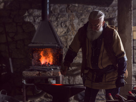 A Viking blacksmith with a white beard and braided hair works intently at a forge, hammering glowing...