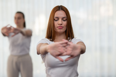 Focused young woman in a white shirt performing a stretching exercise indoors. Concept of wellness,...