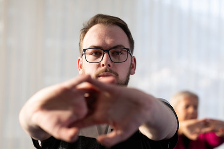 Man stretching his arms forward during a fitness or rehabilitation class indoors. Concept of focus, mindfulness, health, and active lifestyle.の写真素材