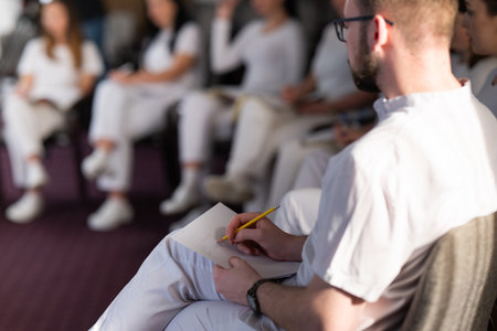 Close up of a student holding a pen and writing notes in a notebook during a professional training and education session in a wellness and therapy courseの写真素材