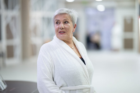Portrait of a senior woman wearing a white bathrobe at a wellness center, symbolizing relaxation, self-care, and healthy aging lifestyle.の写真素材