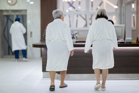 Elderly women walking together in a wellness and spa center dressed in white bathrobes, symbolizing relaxation, friendship, and healthy lifestyle.の写真素材