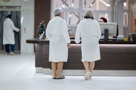 Elderly women walking together in a wellness and spa center dressed in white bathrobes, symbolizing relaxation, friendship, and healthy lifestyle.の写真素材