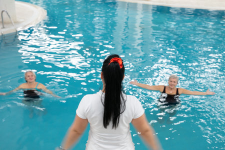 Instructor leading aquatic fitness training for group senior women in a swimming pool. Concept of health, exercise, wellness, water therapy, and active aging lifestyleの写真素材