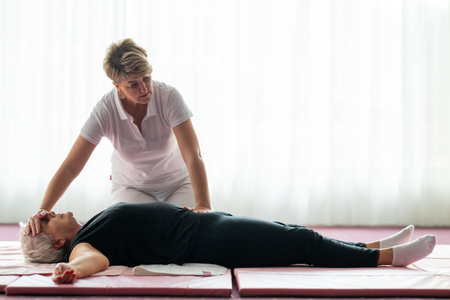 Professional female physiotherapist assisting an older woman lying on a mat during a therapeutic rehabilitation session. Wellness and physiotherapy concept highlighting recovery, mobility, pain relief, and holistic healthcare.の写真素材