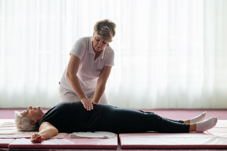 Professional female physiotherapist assisting an older woman lying on a mat during a therapeutic rehabilitation session. Wellness and physiotherapy concept highlighting recovery, mobility, pain relief, and holistic healthcare.の写真素材