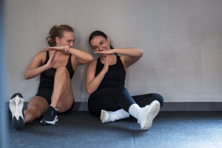 Friends enjoy a moment of laughter while resting after an intense workout session in a fitness studioの写真素材