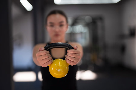Woman using a kettlebell during a strength training session at a gym in the late afternoonの写真素材