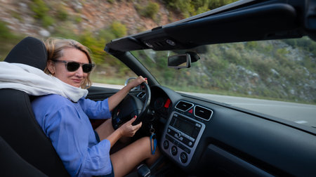 Young woman driving convertible along scenic ocean coast and mountain road at sunset, carefree...