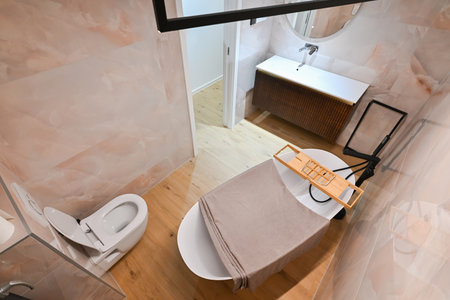 Luxurious modern bathroom featuring a sleek freestanding bathtub with a caddy, elegant vanity with sink and mirror, and a contemporary toilet. Soft tiled walls and wooden flooring create a spa-like, tranquil atmosphereの写真素材