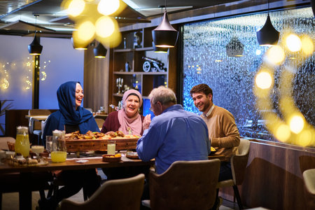 Muslim family gathering for iftar in a restaurant with Ramadan decorations and warm lightingの写真素材