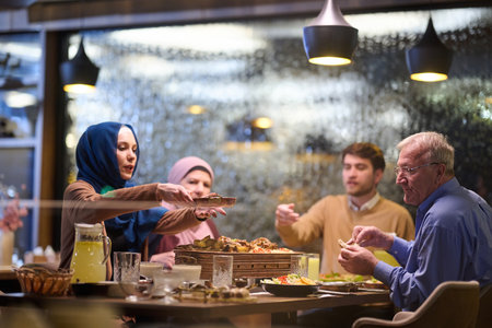 Muslim family breaks fast during Ramadan in a cozy restaurant setting with festive decorationsの写真素材