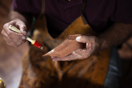Artisan hand paints leather piece with brush, crafting detailed leatherwork by hand